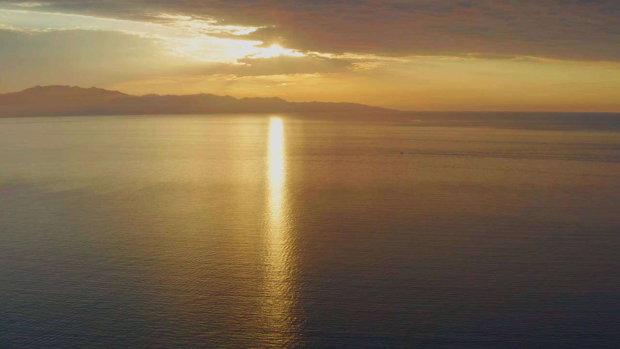 Second frame of the El Sargento La Ventana footage with the sun reflection running down glassy ocean water beneath a dark mountain horizon and no visible people.