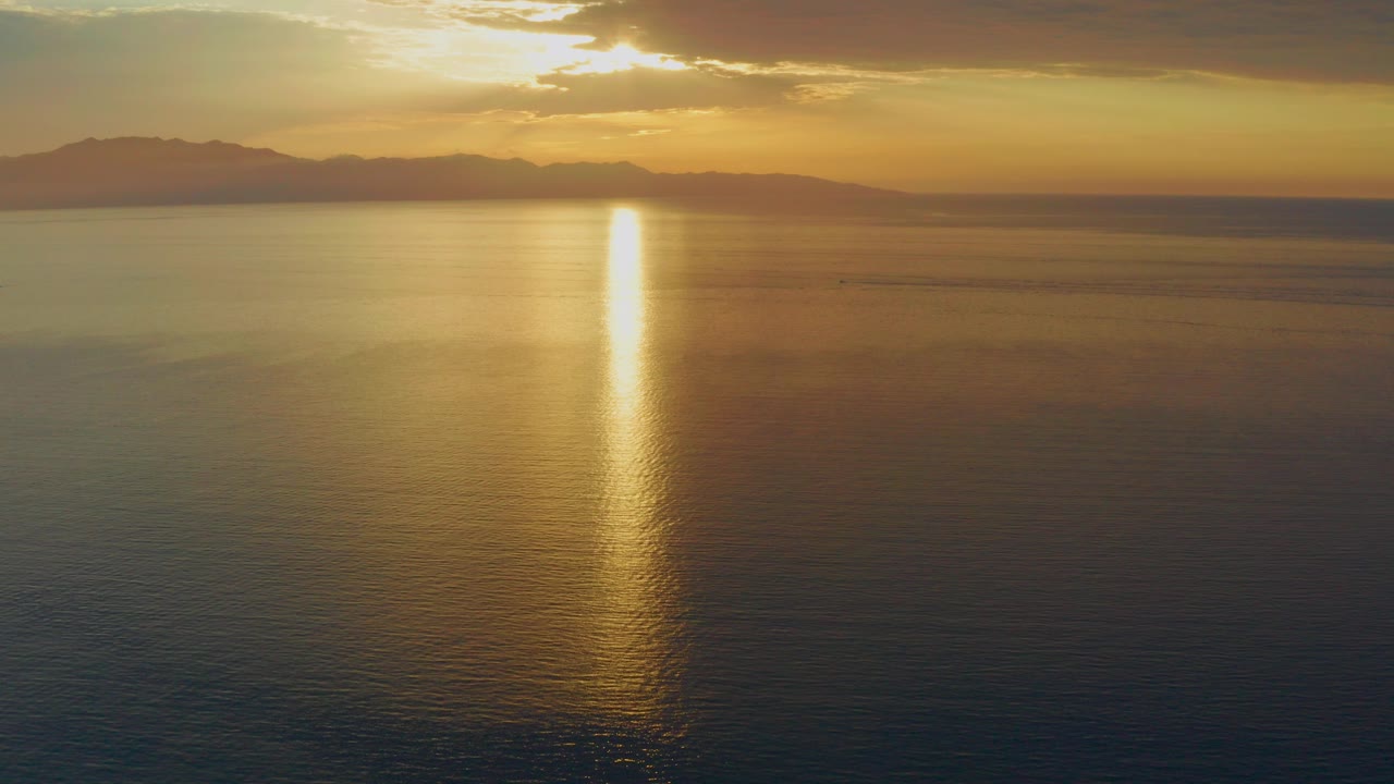 Opening frame of El Sargento La Ventana, Mexico sunset water with a bright vertical sun path, dark distant landforms, thin clouds, and no visible people.