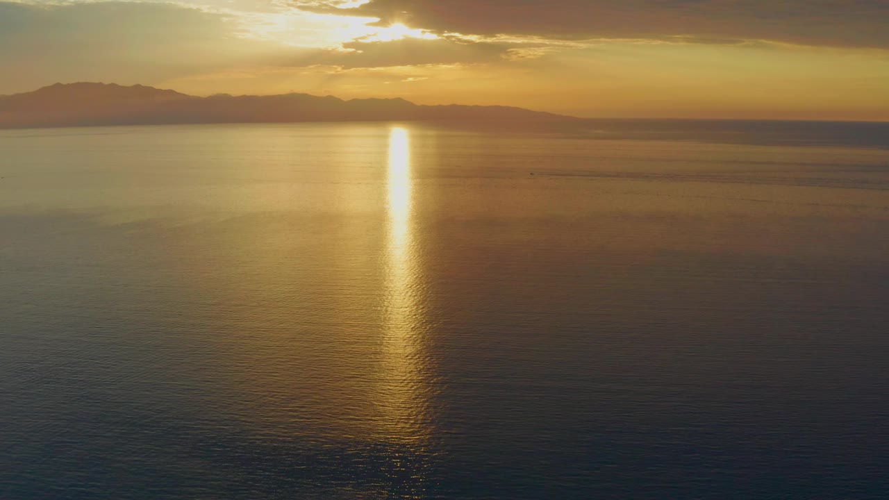 The El Sargento La Ventana water surface darkens toward the foreground while the sunset reflection stays bright under layered clouds, with no visible people.