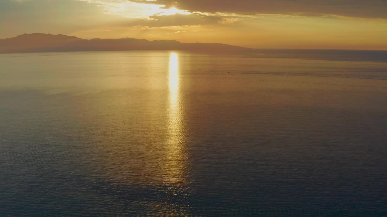 At three seconds, the sun sits partly behind cloud cover above distant land near El Sargento La Ventana, sending a narrow reflection down the water with no visible people.
