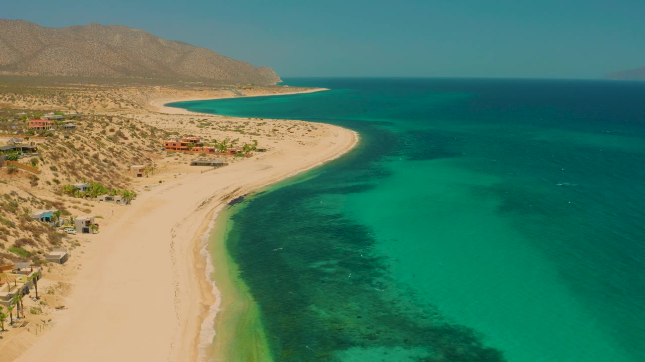 Aerial shoreline frame with beach on the left and clear green water along the coast.