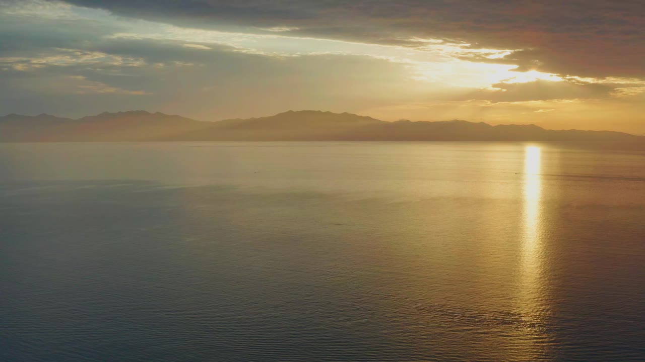 Low sun behind clouds over calm water in El Sargento La Ventana, Mexico, with a gold reflection near the right side and no visible people.