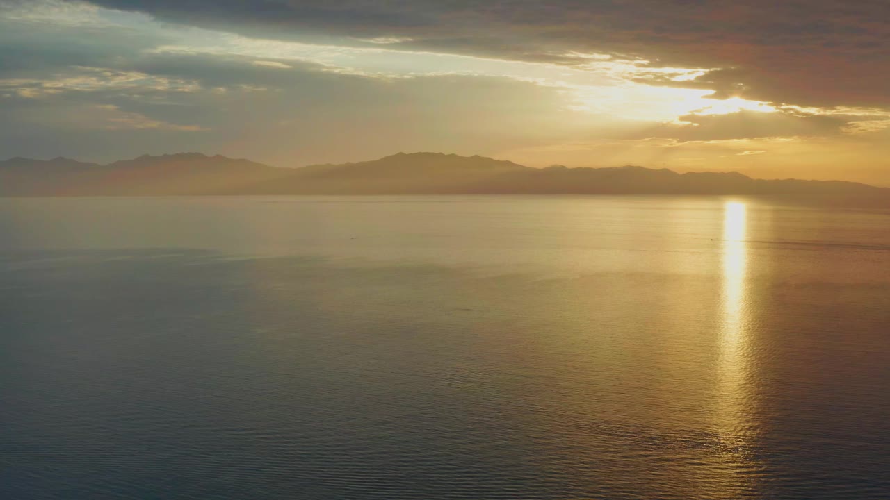 Golden sunlight reflects in a vertical band across open water in El Sargento La Ventana, Mexico, with dark cloud cover above and no visible people.