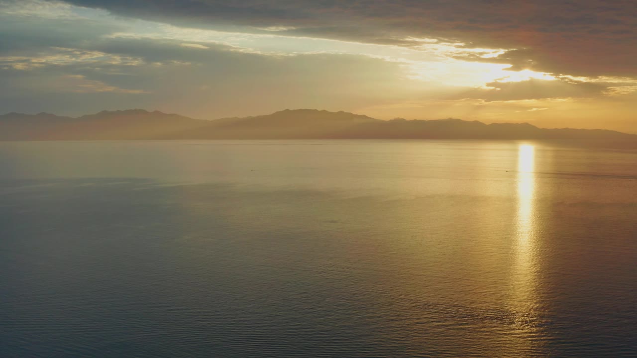A warm sunset sky hangs over distant mountain silhouettes and smooth water in El Sargento La Ventana, Mexico, with no visible people.