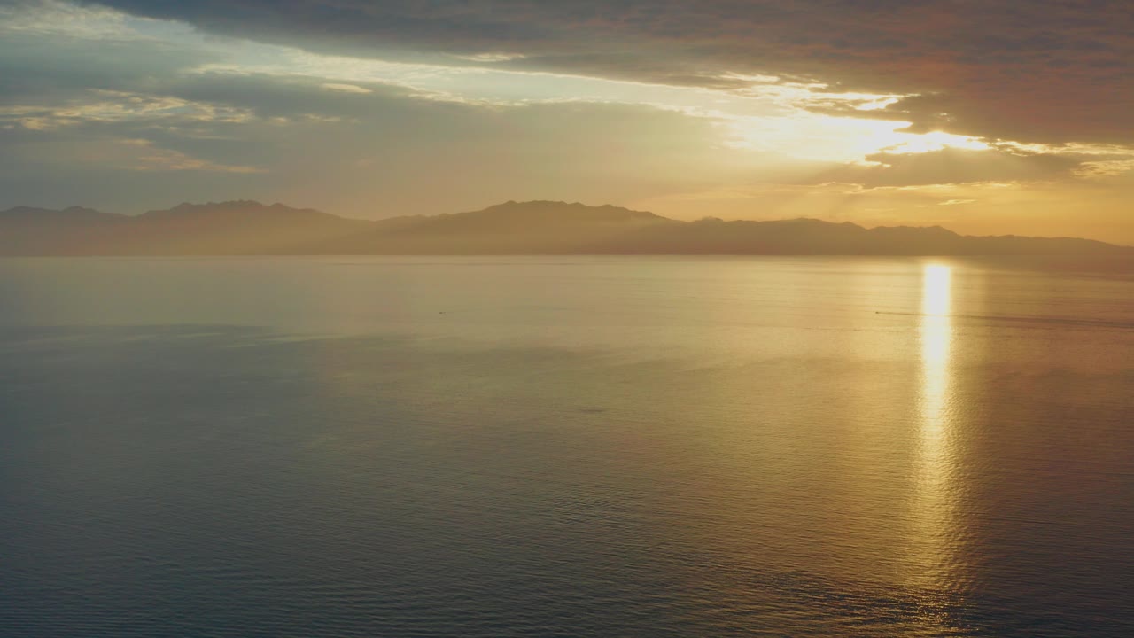 Opening frame of El Sargento La Ventana, Mexico, showing calm water, distant hills, orange cloud light, a bright sun reflection near the right side, and no visible people.