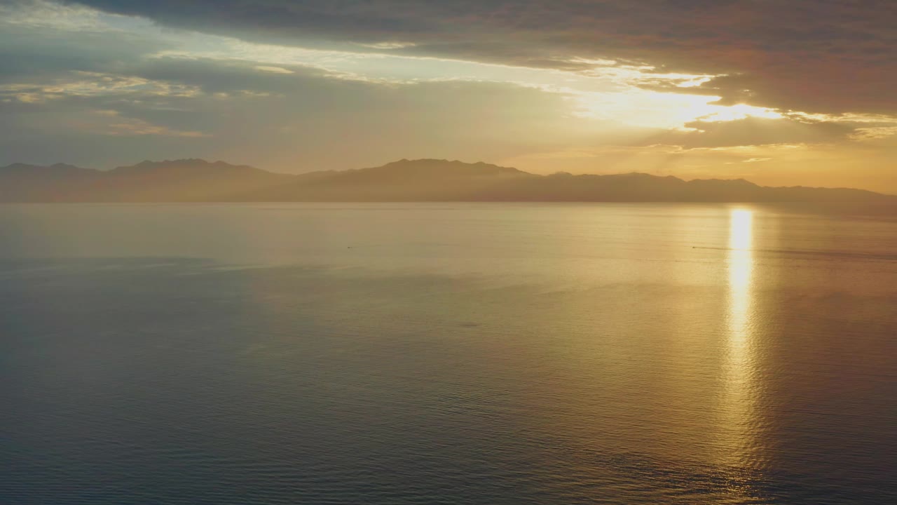 Golden sunset reflection on still water below a clouded sky.