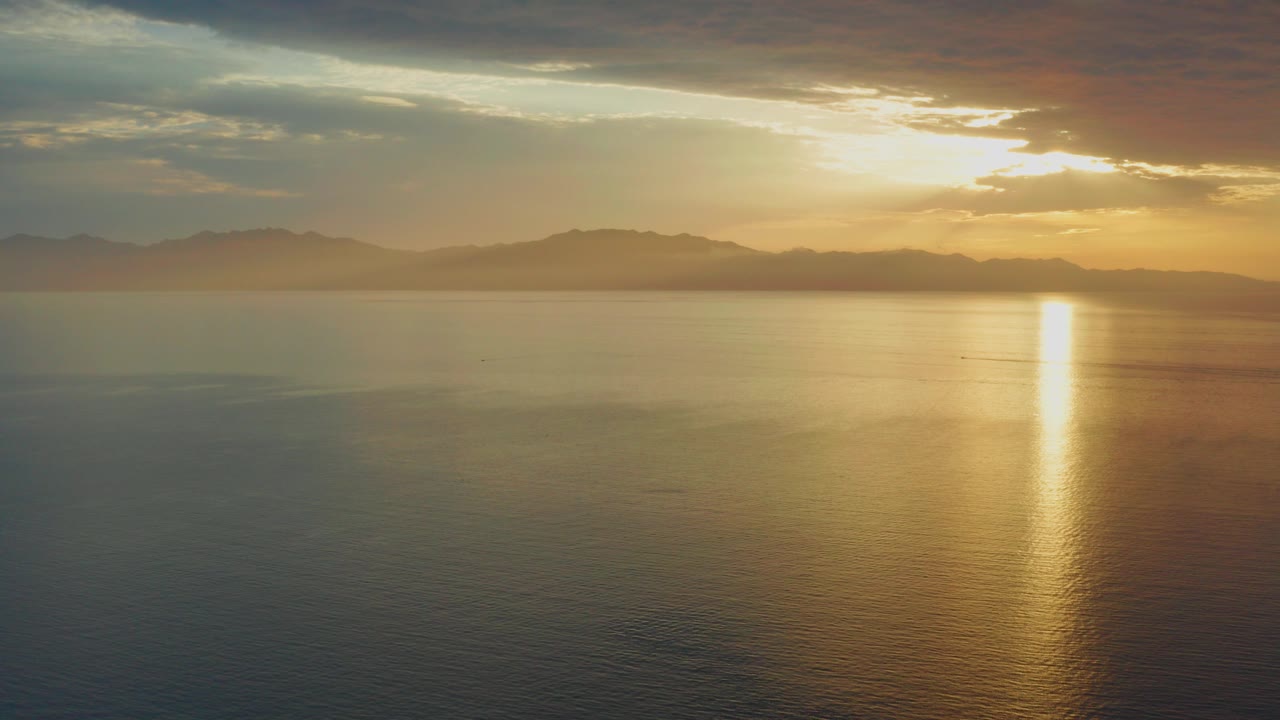 Sunrise reflection over calm water with distant mountains