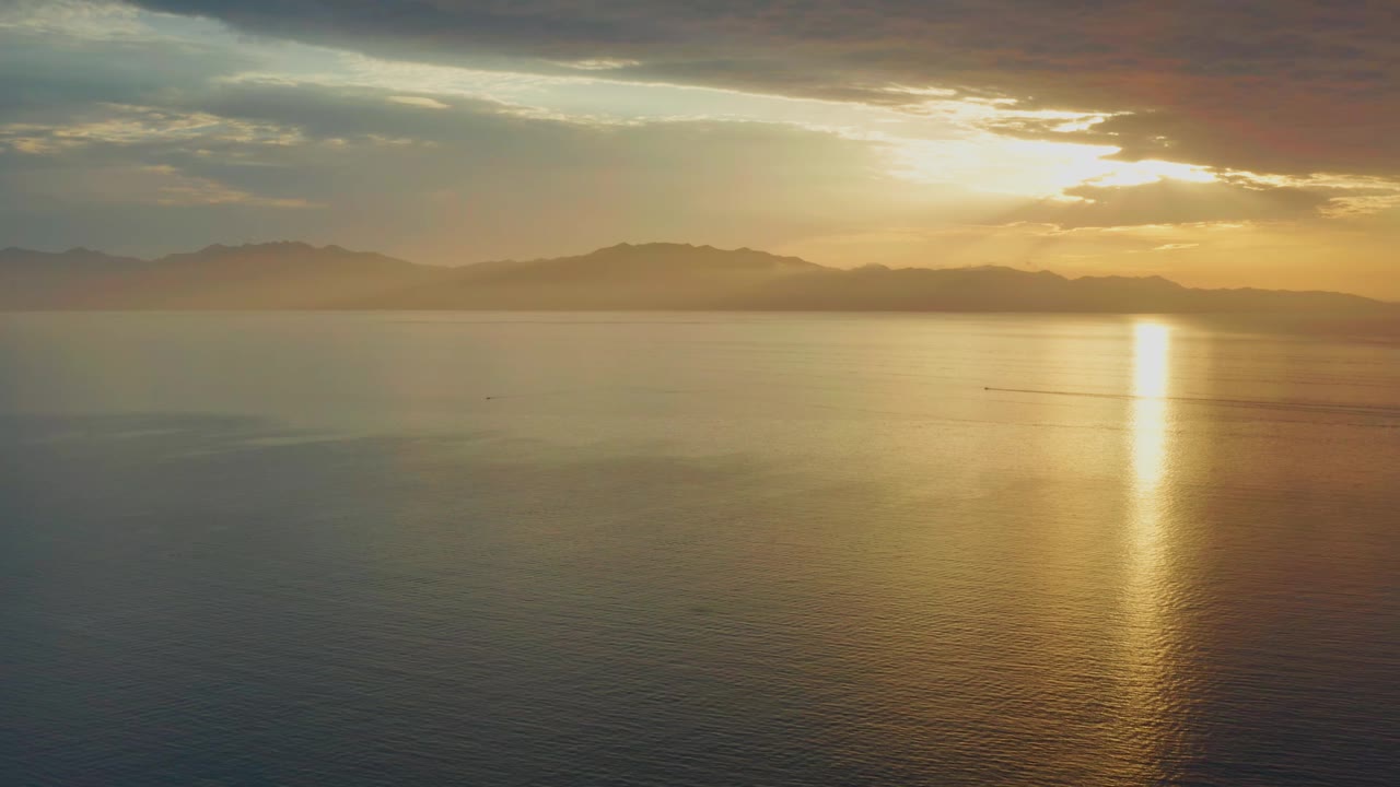 Golden sun sits behind thin cloud over the sea near El Sargento La Ventana, Mexico, with a bright vertical reflection and no visible people.