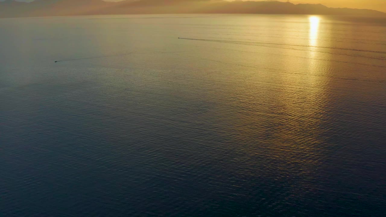 El Sargento La Ventana, Mexico sea surface one second in, with the sun reflection brighter near the upper right, darker ripples below, distant mountains, and no visible people.