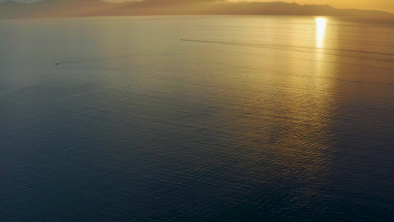 Two seconds into the El Sargento La Ventana, Mexico clip, the frame keeps a high wide view of open sea, gold light on the right, faint wakes across midwater, and no visible people.