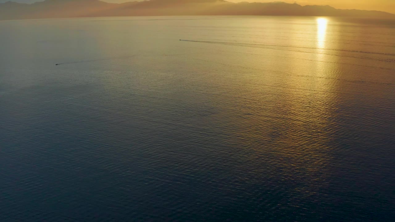 Mid-clip frame from El Sargento La Ventana, Mexico, showing darker foreground water, a gold reflection stretching down from the sun, hazy horizon land, and no visible people.