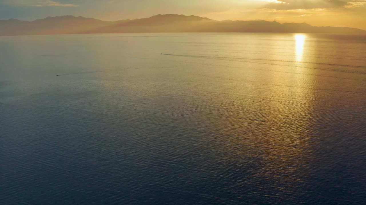A later aerial frame in El Sargento La Ventana, Mexico, shows the bright reflection shifting farther right, with dark water in the foreground, low mountains in the distance, and no visible people.