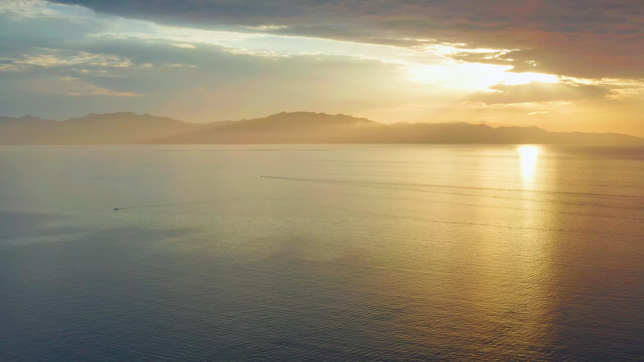 Golden sunset reflection across open water and mountain horizon.