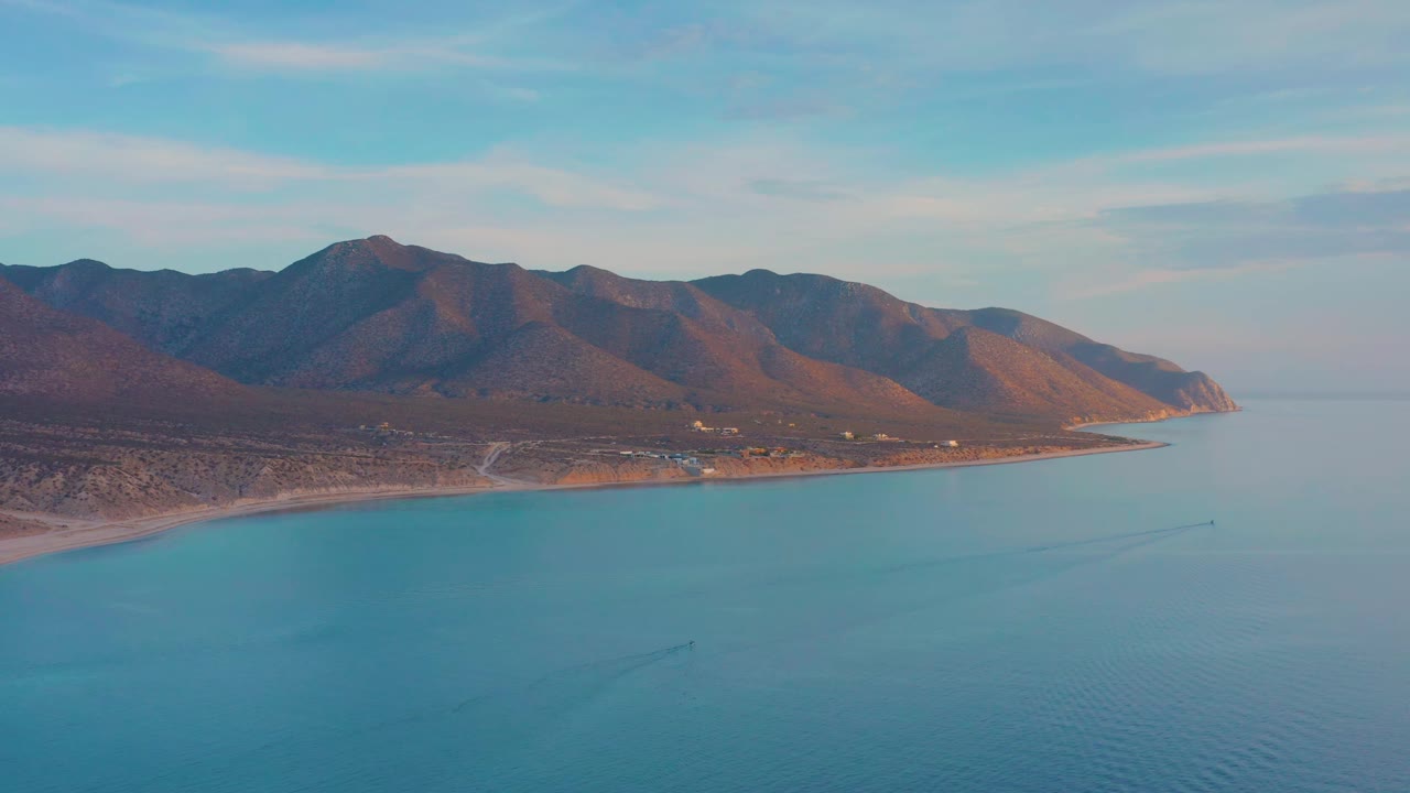 Blue water and a curving shoreline below brown mountain ridges.