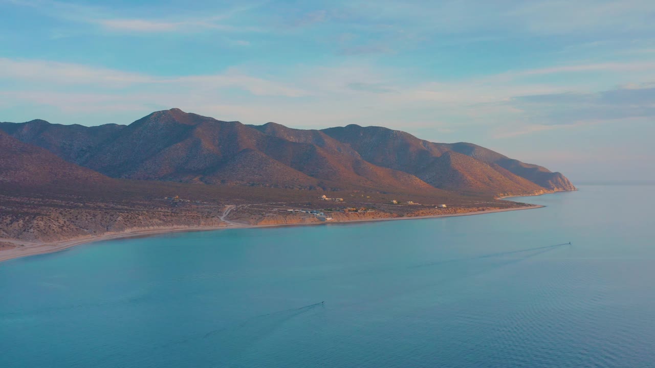 Coastal water in front of brown hills with light clouds above.