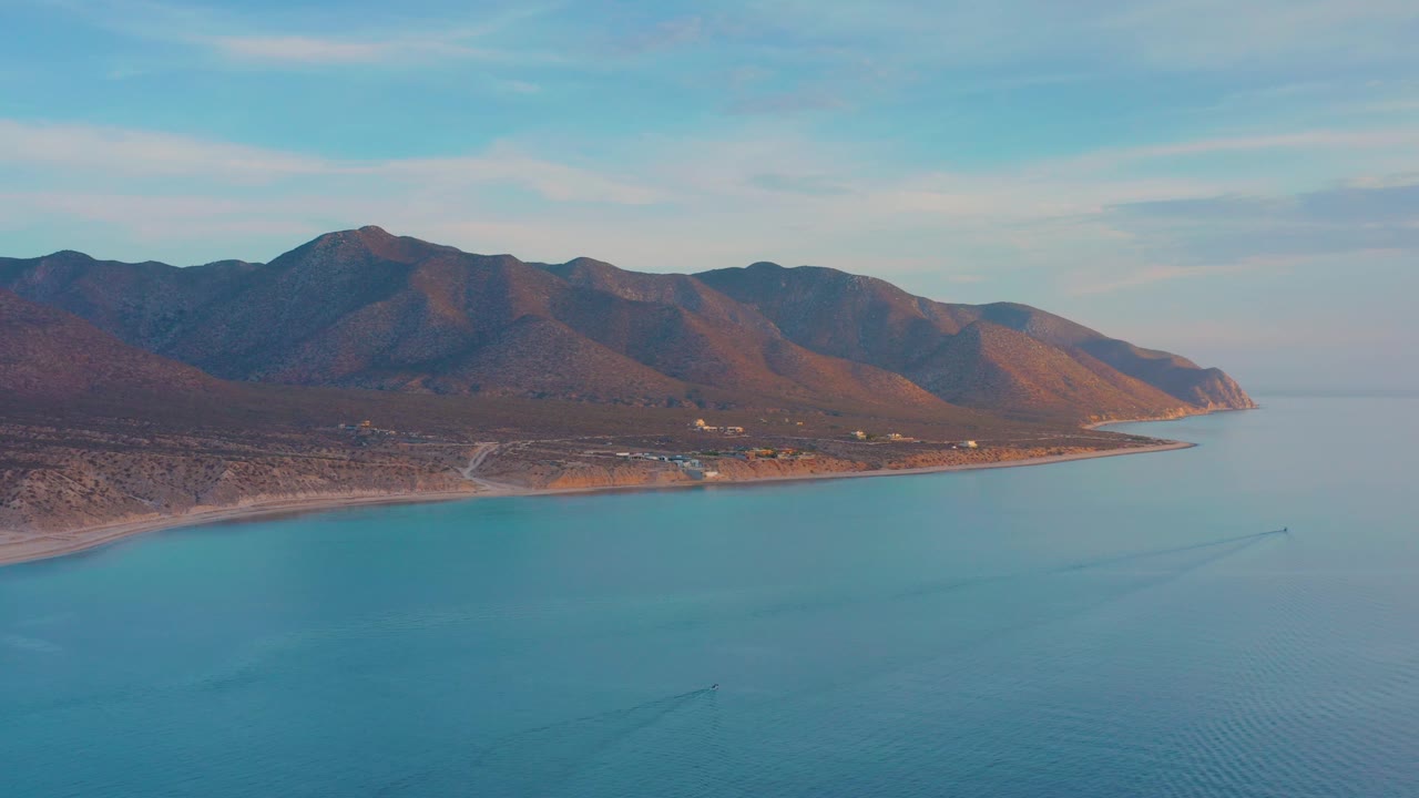 Aerial shoreline below brown mountains and blue sky