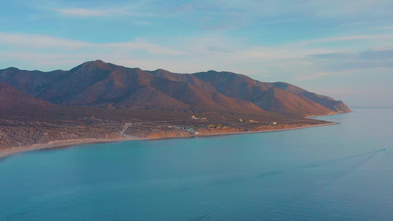 Wide aerial view of coastline, calm water, and mountain ridge.