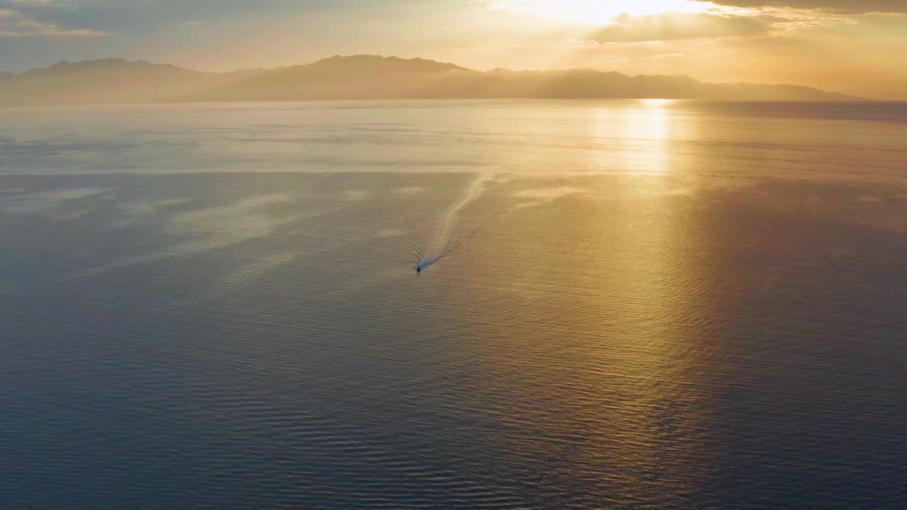 The boat sits slightly farther across the open water in El Sargento La Ventana, Mexico, trailing a narrow wake under a bright gold path of sunlight with no visible people.