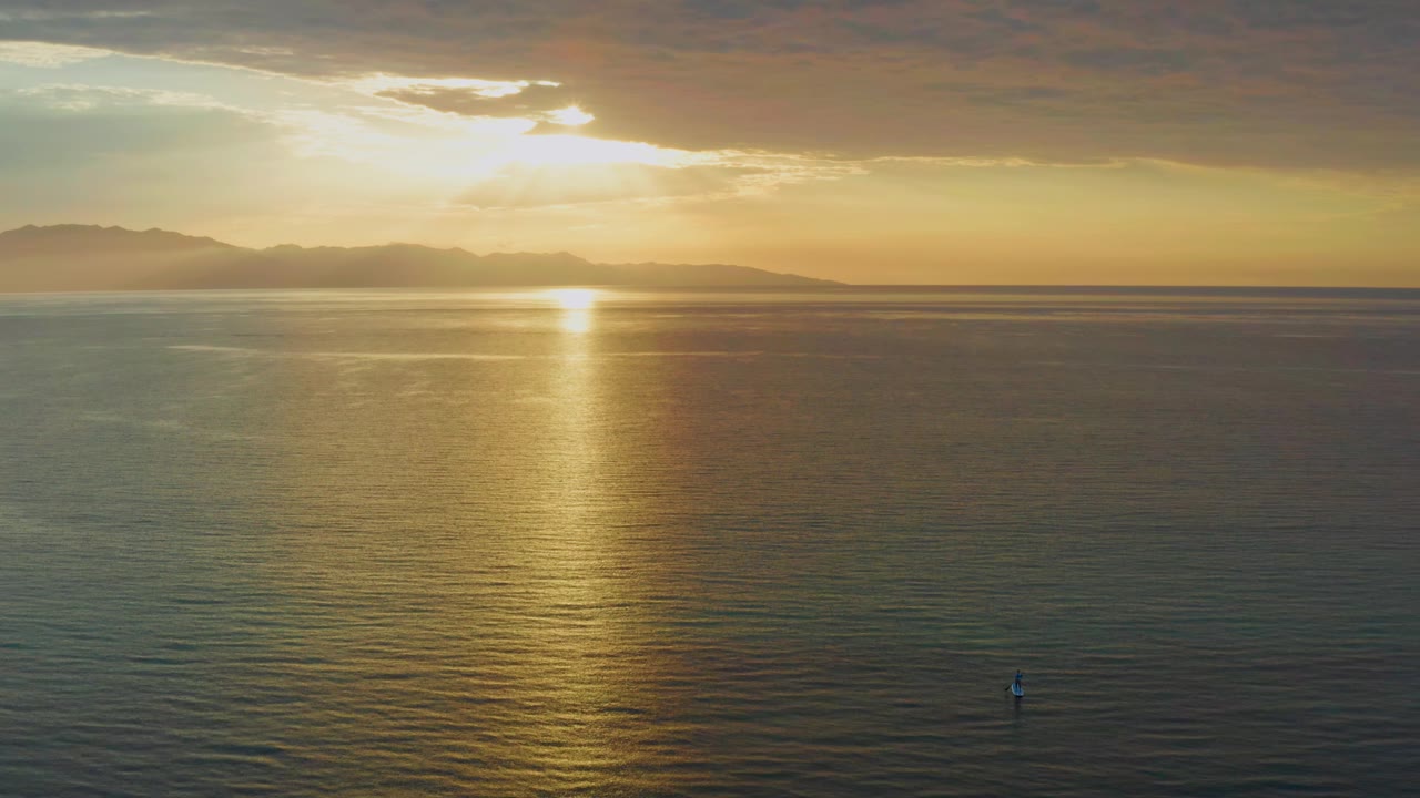 Low sun and golden reflection across ocean water with a tiny figure near the lower frame.