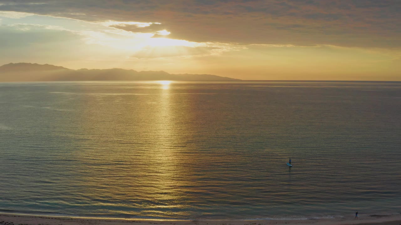 A wide coastal sunset view at El Sargento La Ventana, Mexico, shows the gold reflection widening on the water while the beach remains a thin foreground strip.
