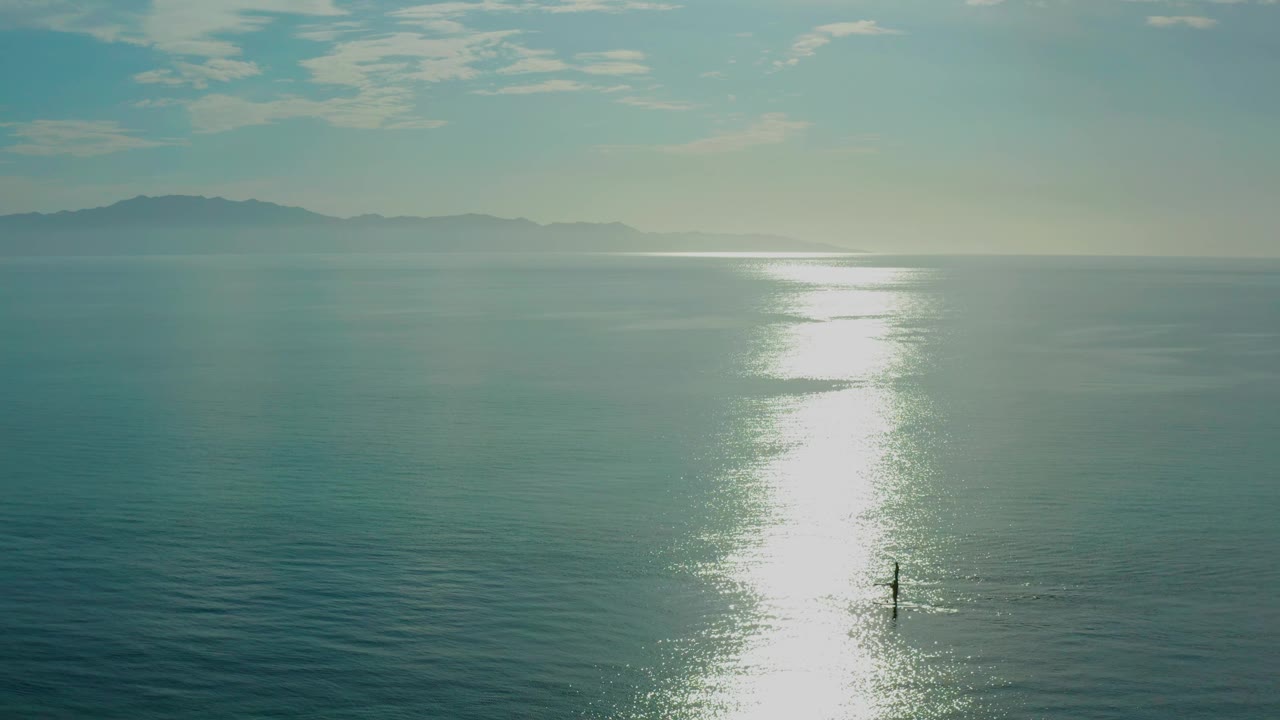 El Sargento La Ventana ocean view with the reflected sun shifted high and right, distant land on the horizon, and the lone sandbar figure near the lower center.