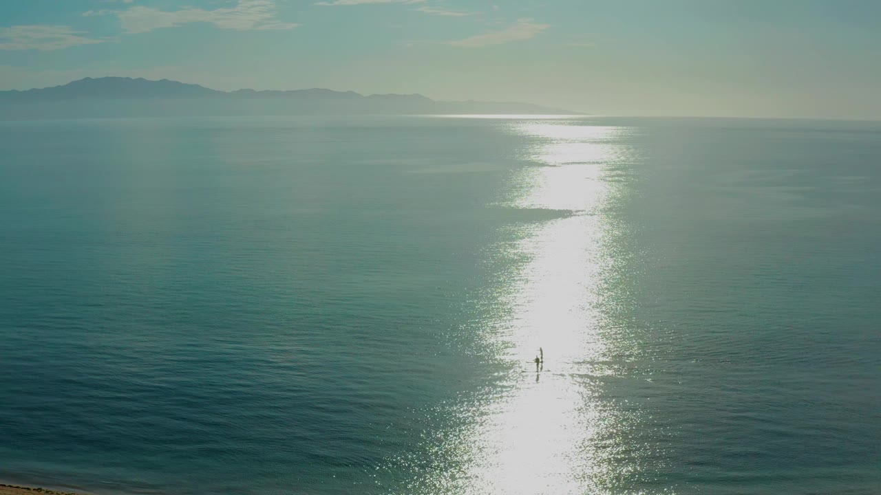 At 0:02, the bright reflection falls slightly right of center on rippled water, with distant landforms above and no identifiable people in the frame.