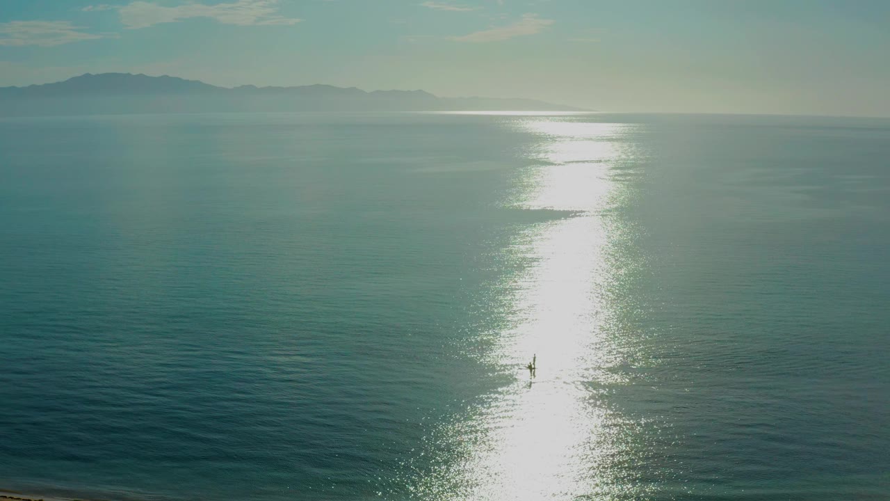 Ocean surface with a long bright reflection and faint beach edge.