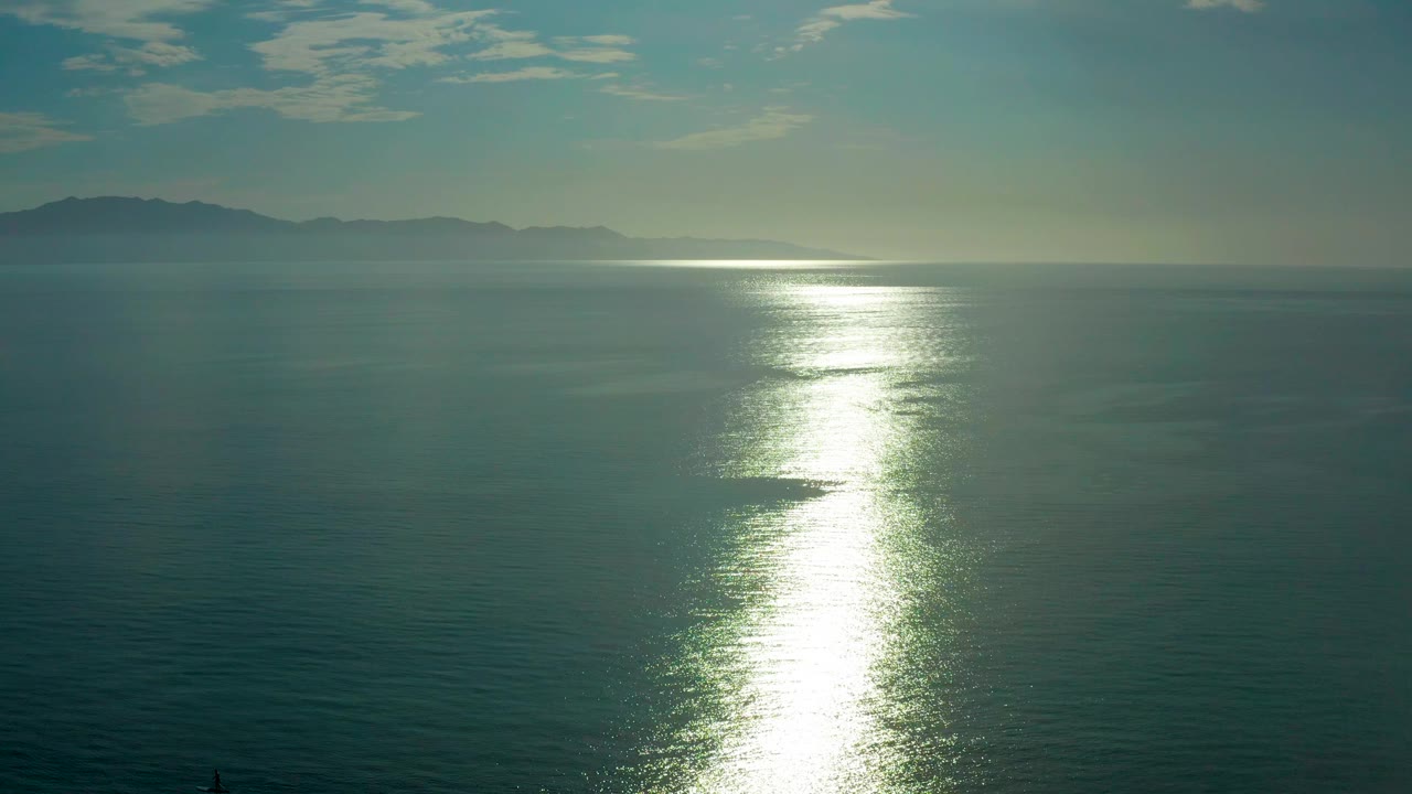 Mid-clip frame from El Sargento La Ventana, Mexico with the sun reflection widening on the ocean surface below muted mountains and no visible people.