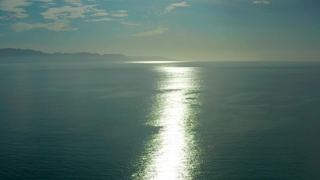Low hazy coastline beyond open water with sunlight reflection