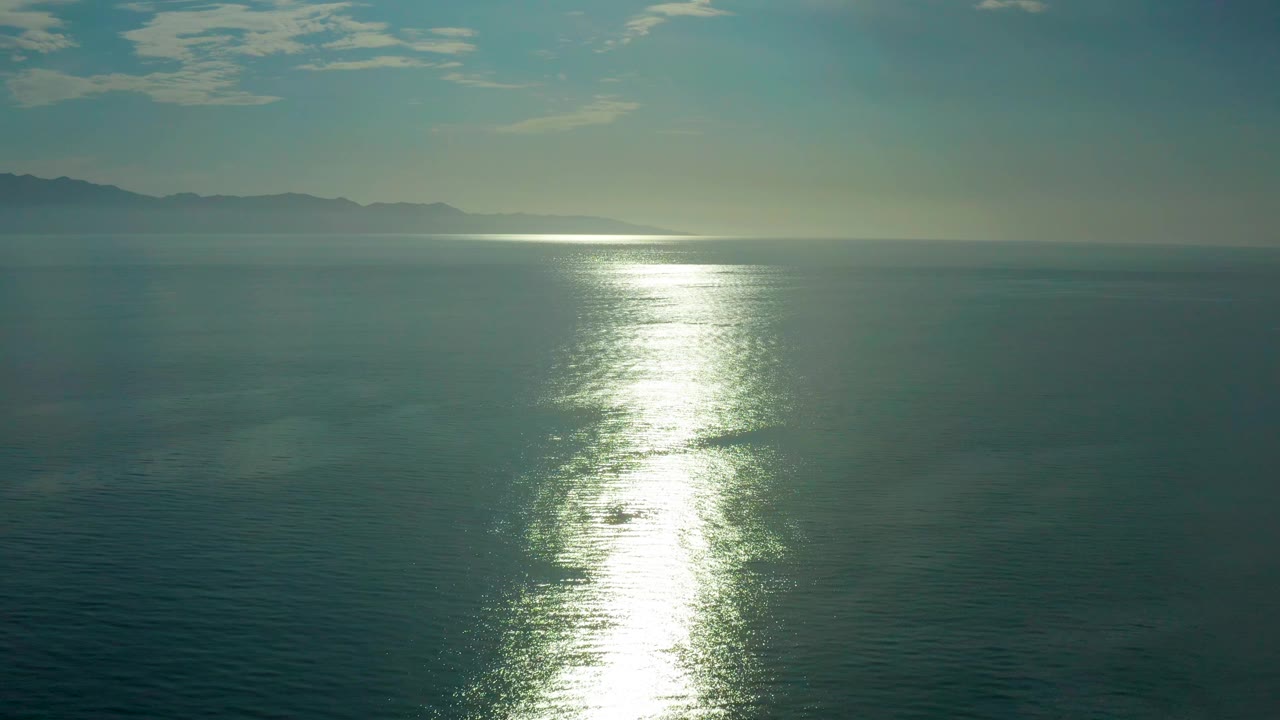 At 0:03 the sun reflection sits slightly left of center on calm water, with the distant mountain line still visible along the left horizon and no visible people.
