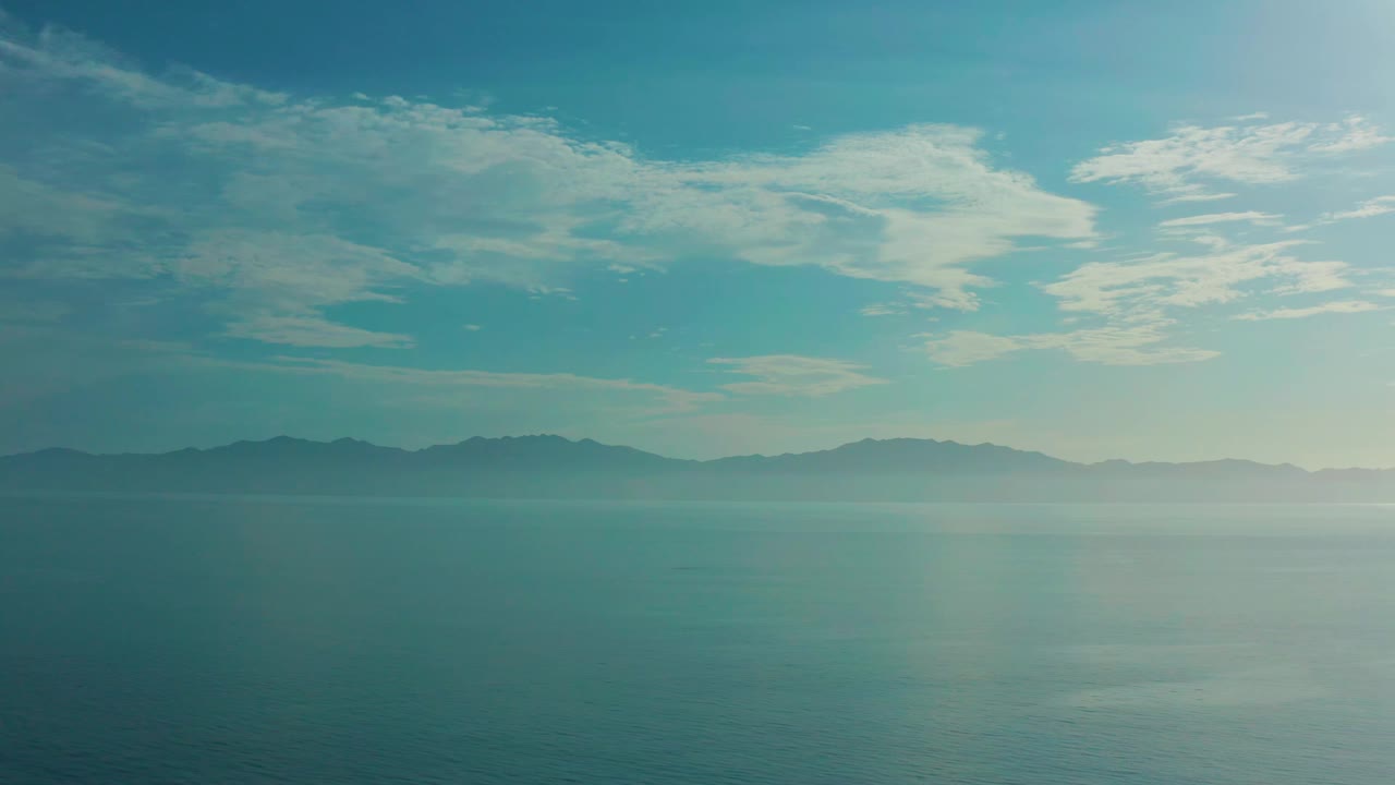 Wide view over calm blue water toward shadowed hills in El Sargento La Ventana, Mexico, with scattered white clouds and no visible people.