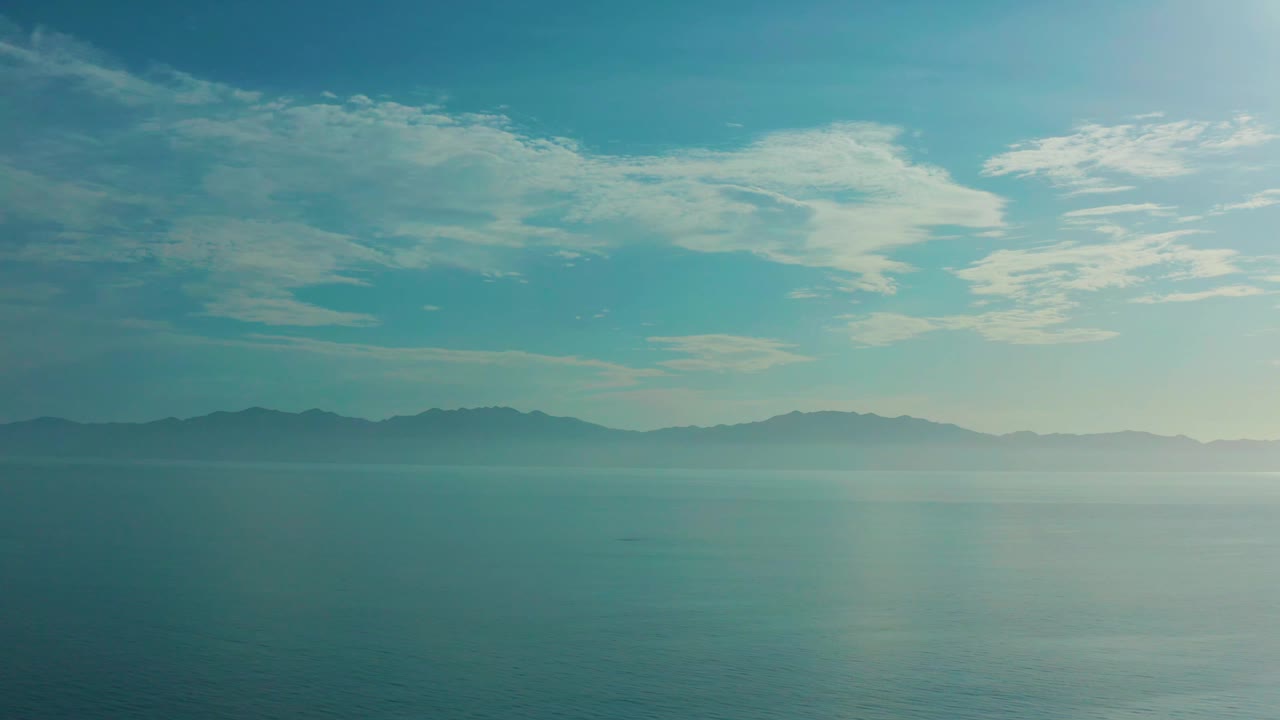 Calm sea with distant dark hills under bright clouds