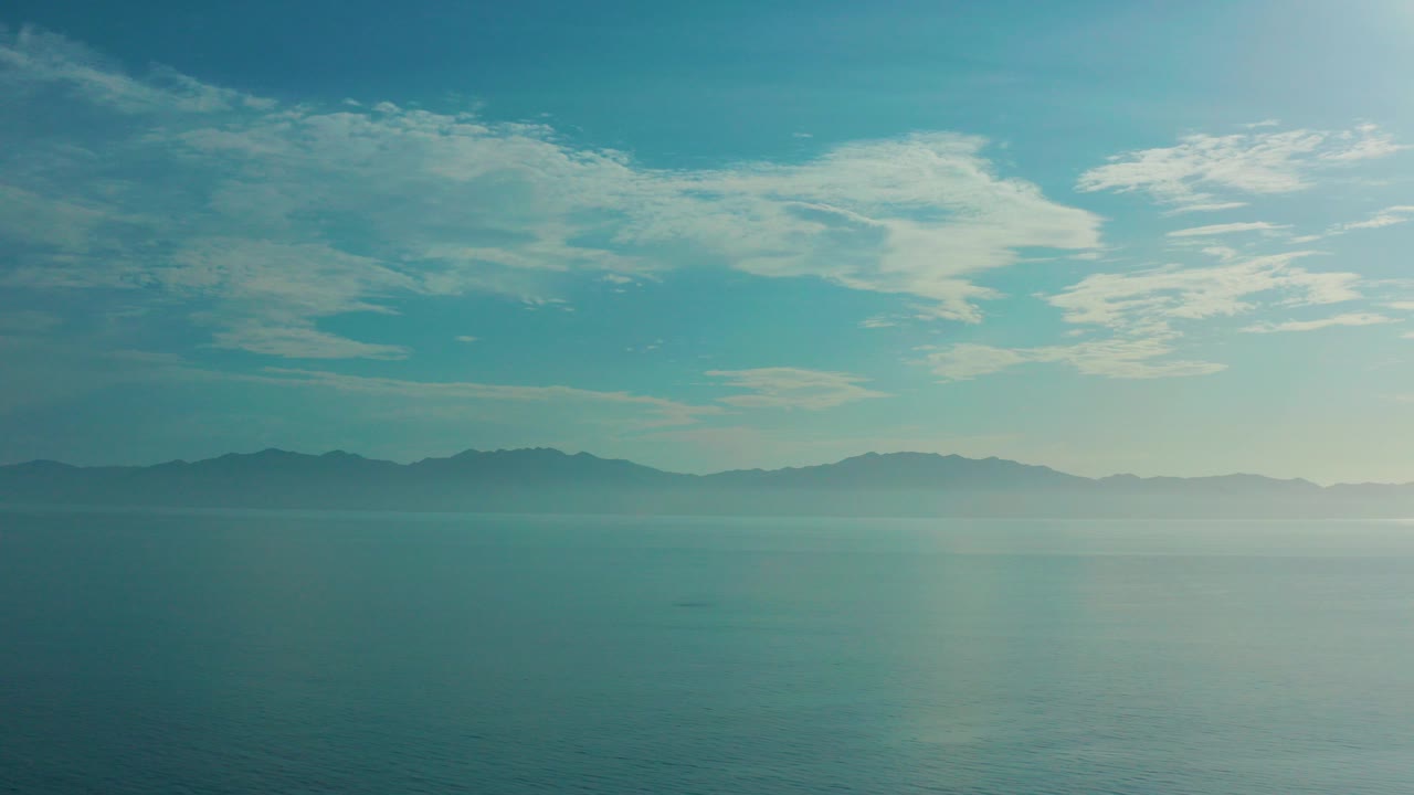Opening frame of El Sargento La Ventana, Mexico with calm blue water, a hazy mountain horizon, high clouds, and no visible people.