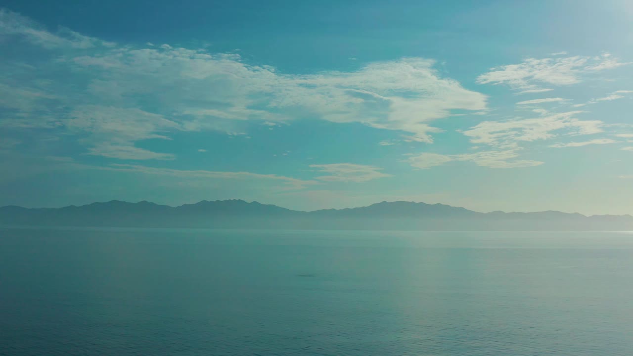 At 0:01, the El Sargento La Ventana view holds on open water, low dark mountain silhouettes, pale haze near the horizon, and layered white clouds with no visible people.