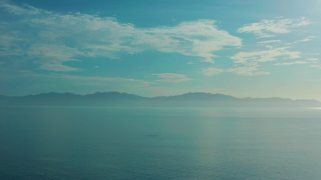 Blue-green sea and low hazy land beneath streaked clouds