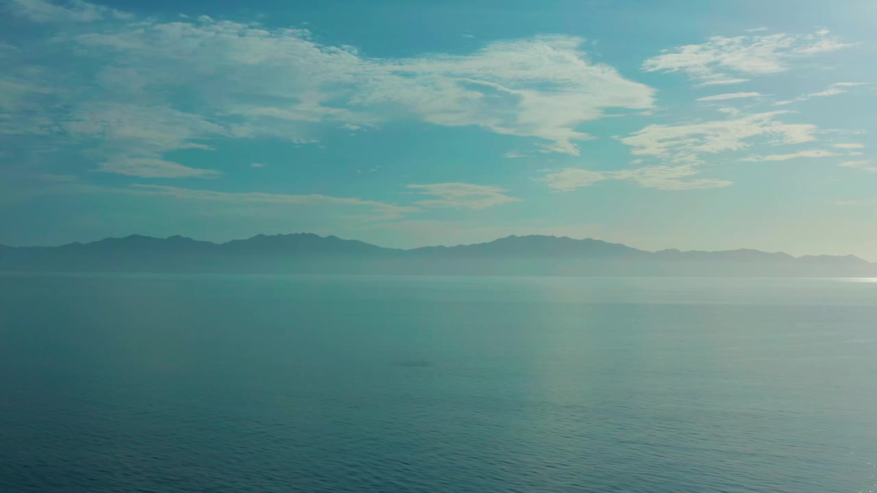 Calm sea in El Sargento La Ventana, Mexico, seen from a high wide angle with mountain silhouettes across the horizon and a brighter patch of water at right, with no visible people.
