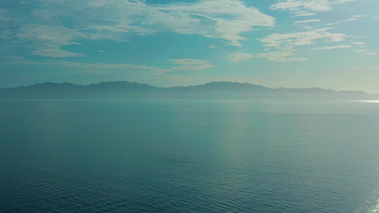 Opening frame of El Sargento La Ventana, Mexico, showing calm blue-green ocean, distant dark mountain ridges, soft cloud cover, and no visible people.