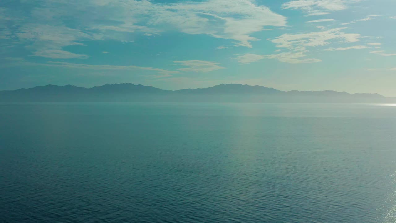 At 0:02, the El Sargento La Ventana view holds on open sea, hazy mountain ridges across the horizon, scattered pale clouds, and no visible people.