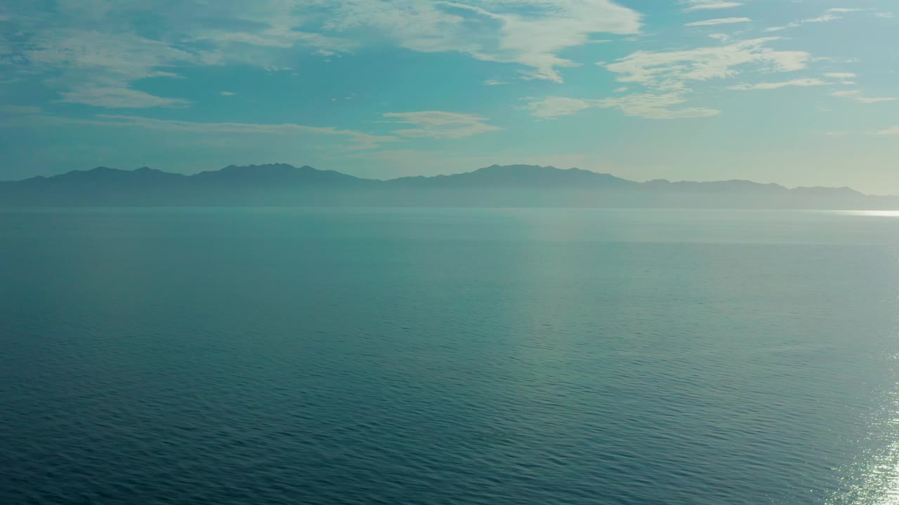 Third frame keeps the horizon high over El Sargento La Ventana, Mexico, with darker ripples in the foreground water, thin haze over the mountains, and no visible people.