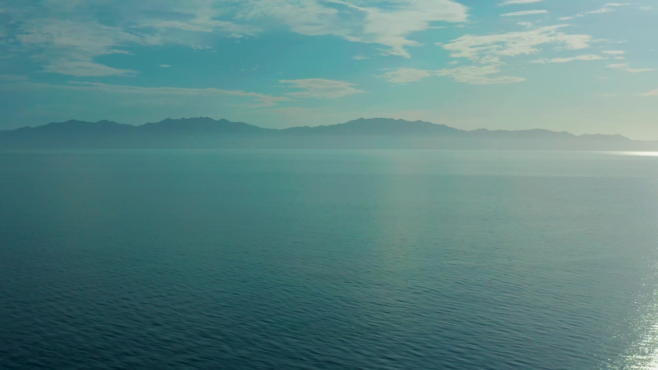 Fourth frame shows broad blue-green water in El Sargento La Ventana, Mexico, with mist softening the mountains and a brighter patch of reflected light near the right edge, with no visible people.