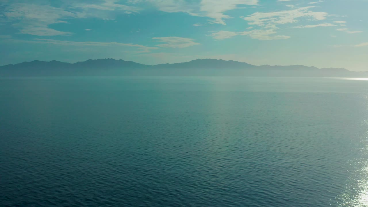 Open blue sea fills the frame near El Sargento La Ventana, Mexico, with a soft haze over distant mountains and a bright reflection along the right side, no visible people.