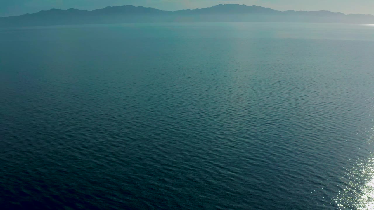 Blue-green ocean fills the frame at El Sargento La Ventana, Mexico, with a bright sun reflection near the lower right edge and no visible people.