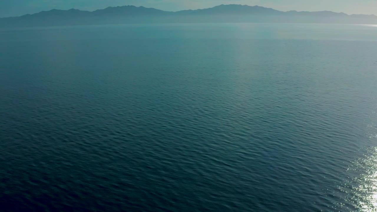 Aerial ocean view at El Sargento La Ventana, Mexico, with textured blue water, mountain silhouettes across the top of frame, and no visible people.