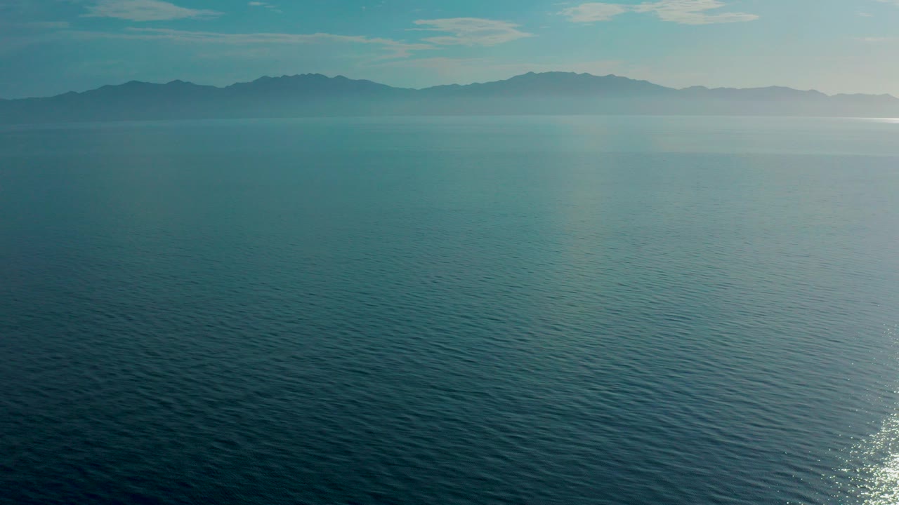 Aerial view over blue-green open water toward hazy mountains in El Sargento La Ventana, Mexico, with no visible people.