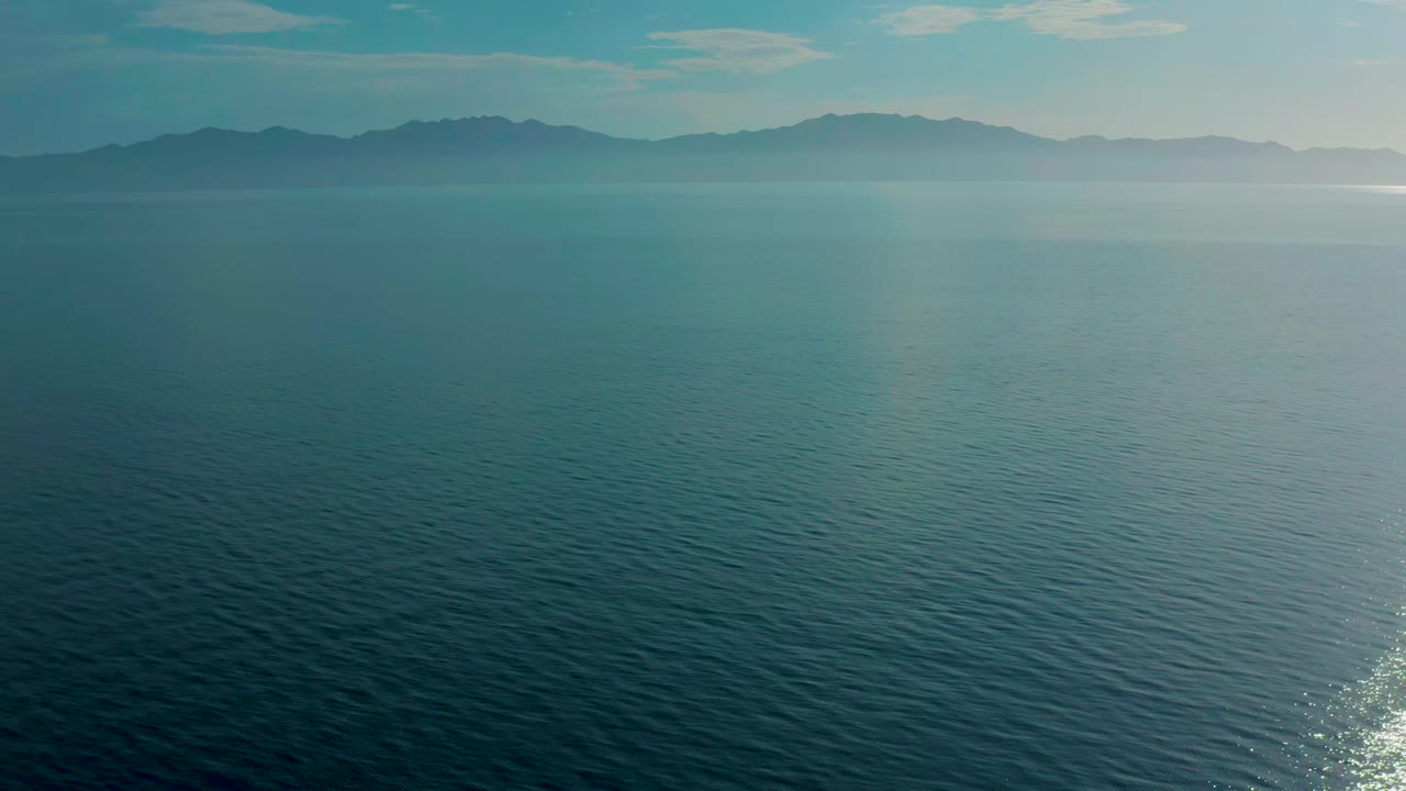 Blue sea fills most of the frame beneath a low hazy mountain horizon in El Sargento La Ventana, Mexico, with no visible people.