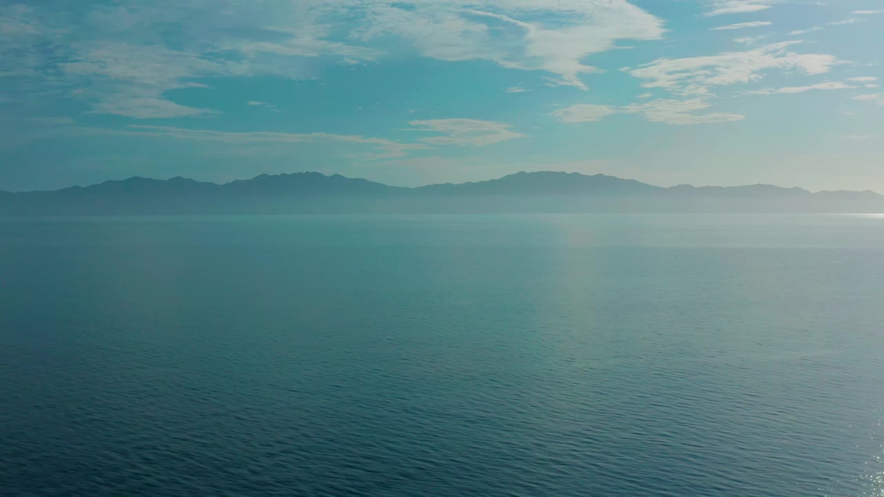Third frame presents blue water in the foreground, a darker mountain ridge to the left and center, brighter haze to the right, and no visible people.