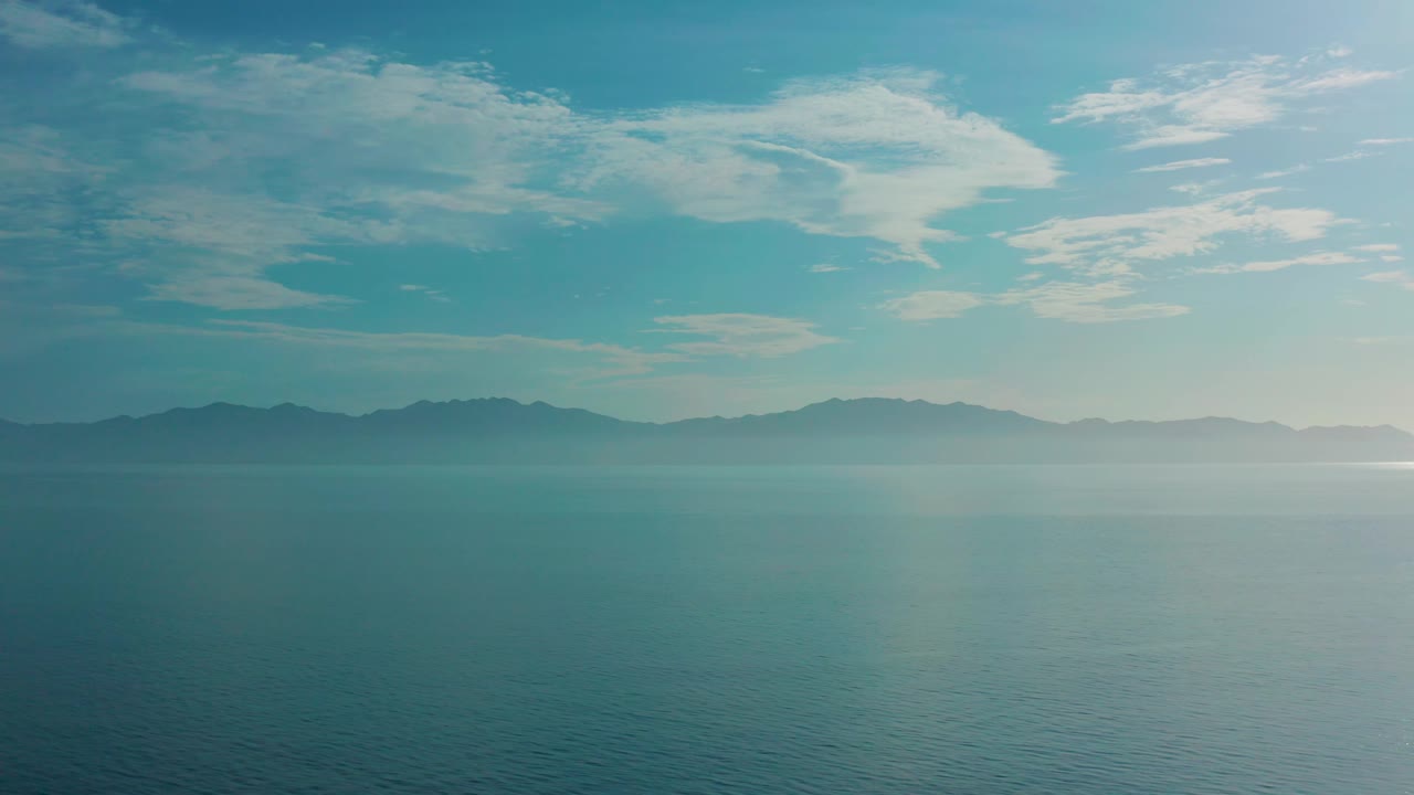 The frame keeps the ocean foreground broad while soft light from the right brightens the water and sky near the mountain range in El Sargento La Ventana, Mexico, with no visible people.