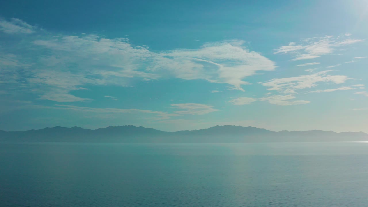 Opening frame of El Sargento La Ventana, Mexico, showing blue-green water beneath a mist-softened mountain horizon and broad blue sky, with no visible people.