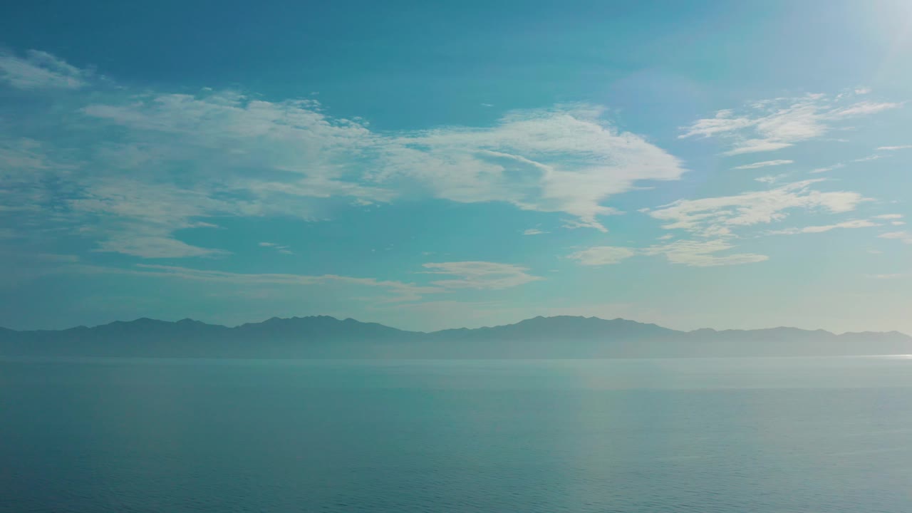 A high view over water in El Sargento La Ventana, Mexico, shows distant mountains softened by mist and a brighter patch of sky near the right edge, with no visible people.