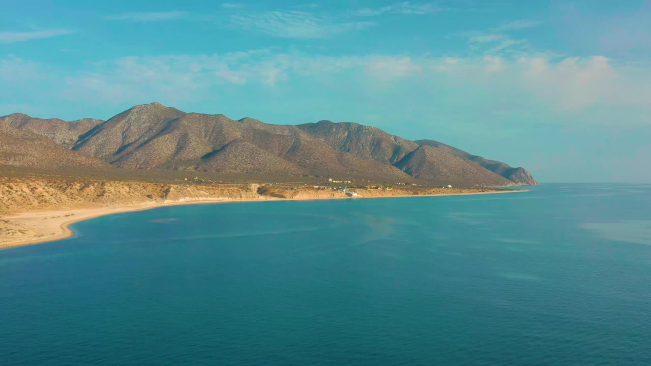 Aerial view of turquoise sea, sandy coast, and brown mountains.